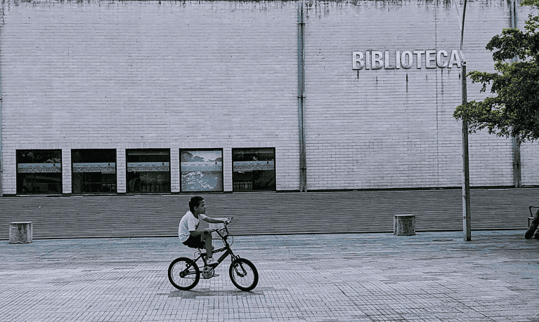Colombian boy ricing bicycle in front of a library.