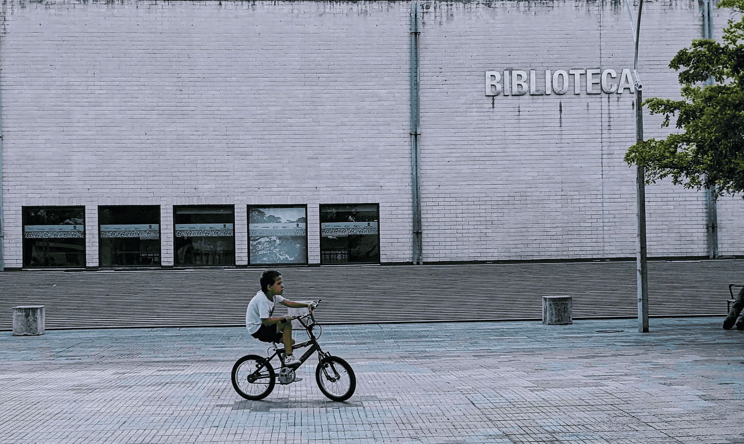 Colombian boy ricing bicycle in front of a library.